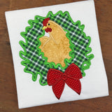 An applique design of a rooster with his head through a Christmas wreath by snugglepuppyapplique.com
