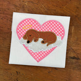 An applique of a dachshund asleep on a cloud with a halo, a heart is in the background by snugglepuppyapplique.com