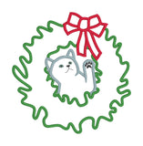 An applique of a cat with its head through a christmas wreath batting at the bow by snugglepuppyapplique.com