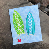 An applique of two surfboards stuck in the sand and an embroidered crab, by snugglepuppyapplique.com