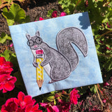 An applique of a squirrel holding a pencil and wearing glasses by snugglepuppyapplique.com