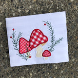 An applique of three woodland mushrooms with embroidered evergreen sprigs and berries by snugglepuppyapplique.com