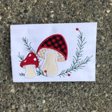 An applique of two mushrooms with embroidered evergreen springs and berries by snugglepuppyapplique.com
