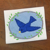 A bean stitch applique of a bird in flight with a frame of twigs and leaves by snugglepuppyapplique.com
