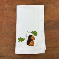 A bean stitch applique of two acorns and two leaves on a cloth napkin  by snugglepuppyapplique.com