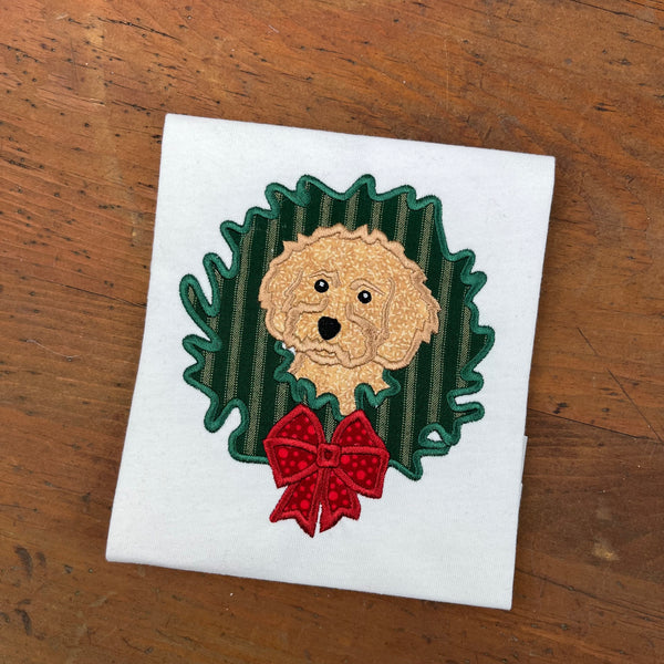 An applique of a Cockapoo dog with its head though a Christmas  wreath in 6 sizes by snugglepuppyapplique.com