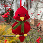 An in the hoop embroidery design of a felt cardinal Christmas ornament. He sits on a real twig and is wearing a scarf.