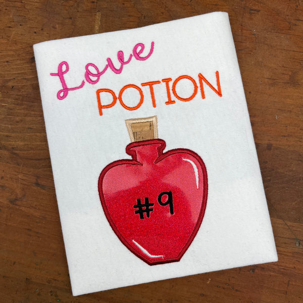 An appliqué of a heart shaped bottle with "# 9" embroidered on it and the words "Love Potion" embroidered above the bottle. by snugglepuppyapplique.com