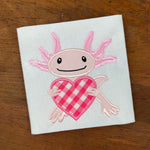 An applique design of an Axolotl holding a heart by snugglepuppyapplique.com