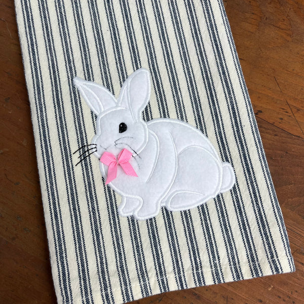 An applique of a white rabbit with a ribbon bow attached by snugglepuppyapplique.com