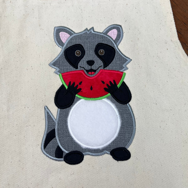 An applique design of a cute Raccoon eating a slice of watermelon by snugglepuppyappliquecom