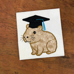 An applique embroidery design of a capybara wearing a graduation cap and tassel by snugglepuppyapplique.com