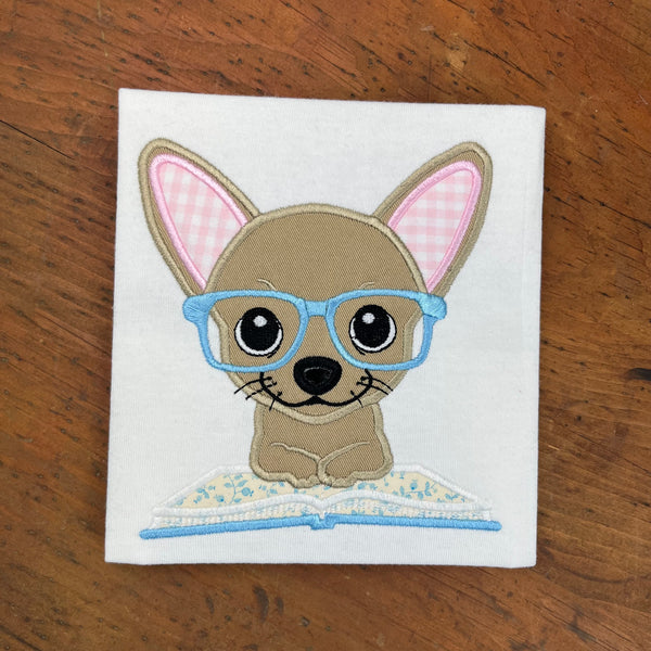 An applique of a chihuahua wearing glasses with his front paws on an open book by snugglepuppyapplique.com