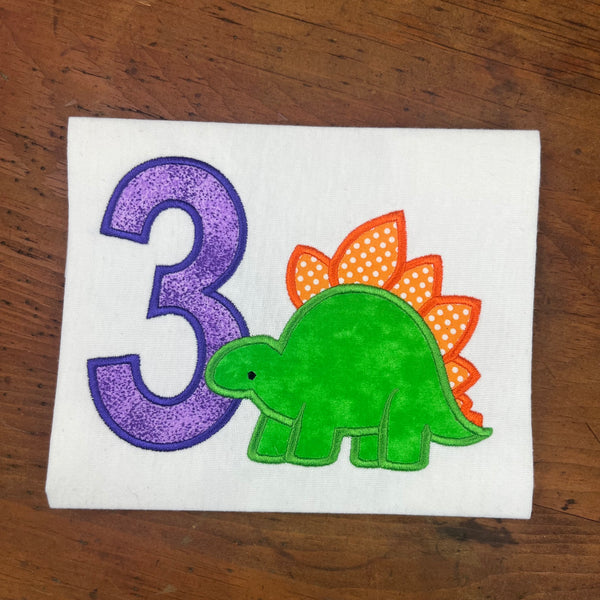 An applique of a stegosaurus
and the number 3 by snugglepuppyapplique.com
