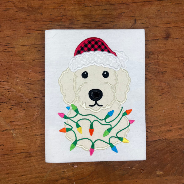 An applique design of a golden doodle dog wearing a Santa hat and wrapped in Christmas lights in 6 sizes by snugglepuppyapplique.com