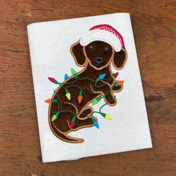 An applique of a dachshund wearing a Christmas hat wrapped in christmas lights by snugglepuppyapplique.com