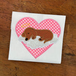 An applique of a dachshund asleep on a cloud with a halo, a heart is in the background by snugglepuppyapplique.com