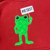 Red sweatshirt with an applique of a green frog holding a 'RESIST' sign on a red background