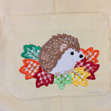 An applique of a hedgehog on a bed of fall leaves by snugglepuppyapplique.com