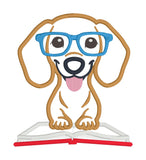 An applique of a dachshund wearing glasses and his paws on an open book by snugglepuppyapplique.com