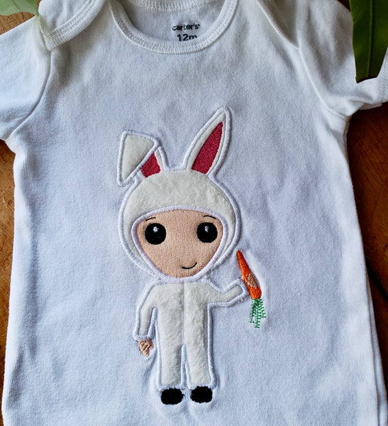 An applique of a cute kid in an Easter Bunny costume holding a carrot by snugglepuppyapplique.com