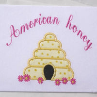 An applique of a beehive with flowers and the words "American honey" embroidered above  by snugglepuppyapplique.com
