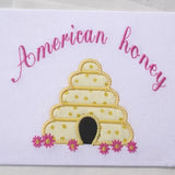 An applique of a beehive with flowers and the words "American honey" embroidered above  by snugglepuppyapplique.com