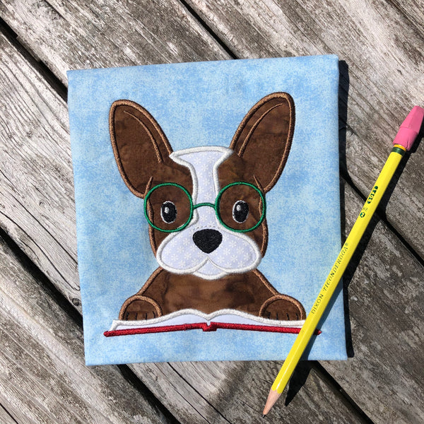 An applique of a French bulldog with his paws on a book and embroidered Glasses on this face by snugglepuppyapplique.com