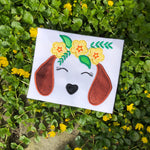 An applique of a dachshund's ears, nose and closed eyes with lashes and wearing a crown of flowers and leaves by snugglepuppyapplique.com