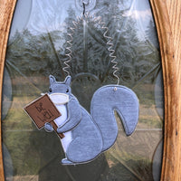 An in the hoop squirrel door hanger with a medical face mask holding a sign that says "Be well" by www.snugglepuppyapplique.com