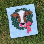A bean stitch applique of a cow with its head through a wreath by snugglepuppyapplique.com