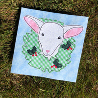 A bean stitch applique of a sheep with it's head stuck through a Christmas wreath by snugglepuppyapplique.com