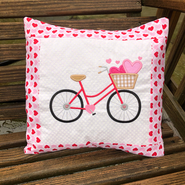 An applique of a bicycle with a basket and two hearts inside it, by snugglepuppyapplique.com