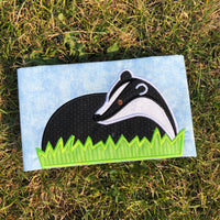 An applique of a badger laying in grass by snugglepuppyappllique.com