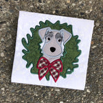 An applique of a Schnauzer dog with its head through a Christmas wreath by snugglepuppyapplique.com