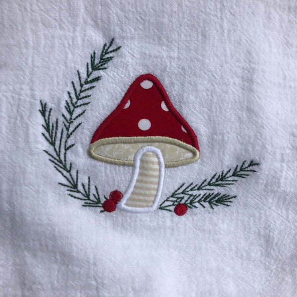 An applique of a mushroom with embroidered evergreen branches and berries by snugglepuppyapplique.com