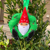 An in the hoop machine embroidery design of a gnome with is head through a holiday wreath and his feet sticking out. by snugglepuppyapplique.com