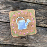 An in the hoop spring coaster with a watering can in the center and a boarder of tulips by snugglepuppyapplique.com