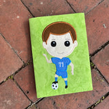 An applique of a soccer player with his foot on a soccer ball by snugglepuppyapplique.com