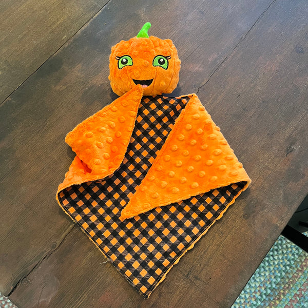 An in the hoop design of a pumpkin with a face attached to a small blanket by snugglepuppyapplique.com