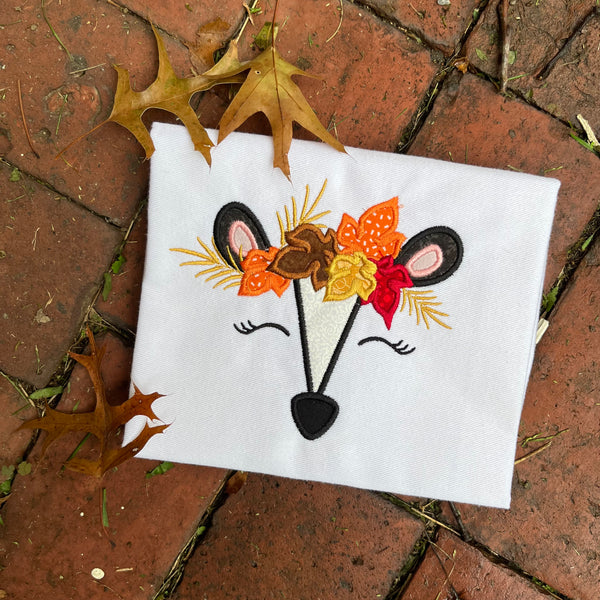 An applique of a skunks face with a autumn leaf crown by snugglpuppyapplique.com