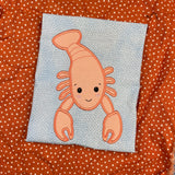 An applique of a babyish lobster embroidery design by snugglepuppyapplique.com  Edit alt text