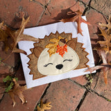 An applique of a sleeping hedgehog with fall leaves and an acorn by snugglepuppyapplique.com
