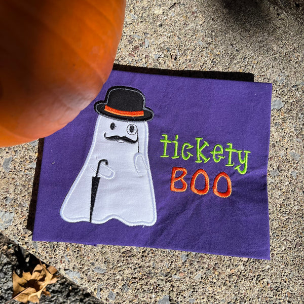 An applique of a ghost with a bowler hat, monocle and umbrella with the words "tickets Boo" embroidered by snugglepuppyapplique.com