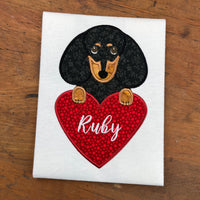 An applique of a Black and Tan dachshund with it's paws on a heart by  snugglepuppyapplique.com