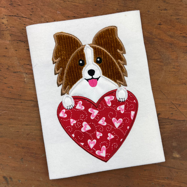 An applique of a papillon with its paws on a heart shape by snugglepuppyapplique.com
