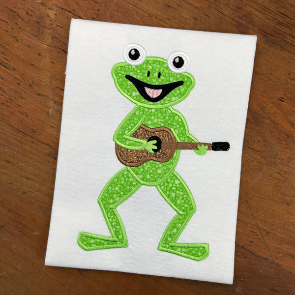 An applique of a frog playing a guitar by snugglepuppyapplique.com