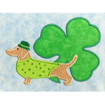 March Dachshund applique embroidery design, dog is wearing hat and coat with shamrock in the background, St. Patrick's day design
